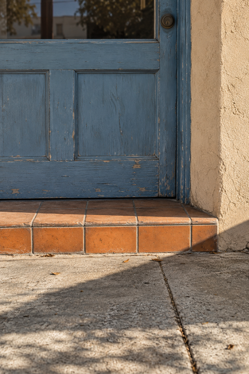 A weathered blue door above terracotta steps, crossed by angled afternoon shadows.
