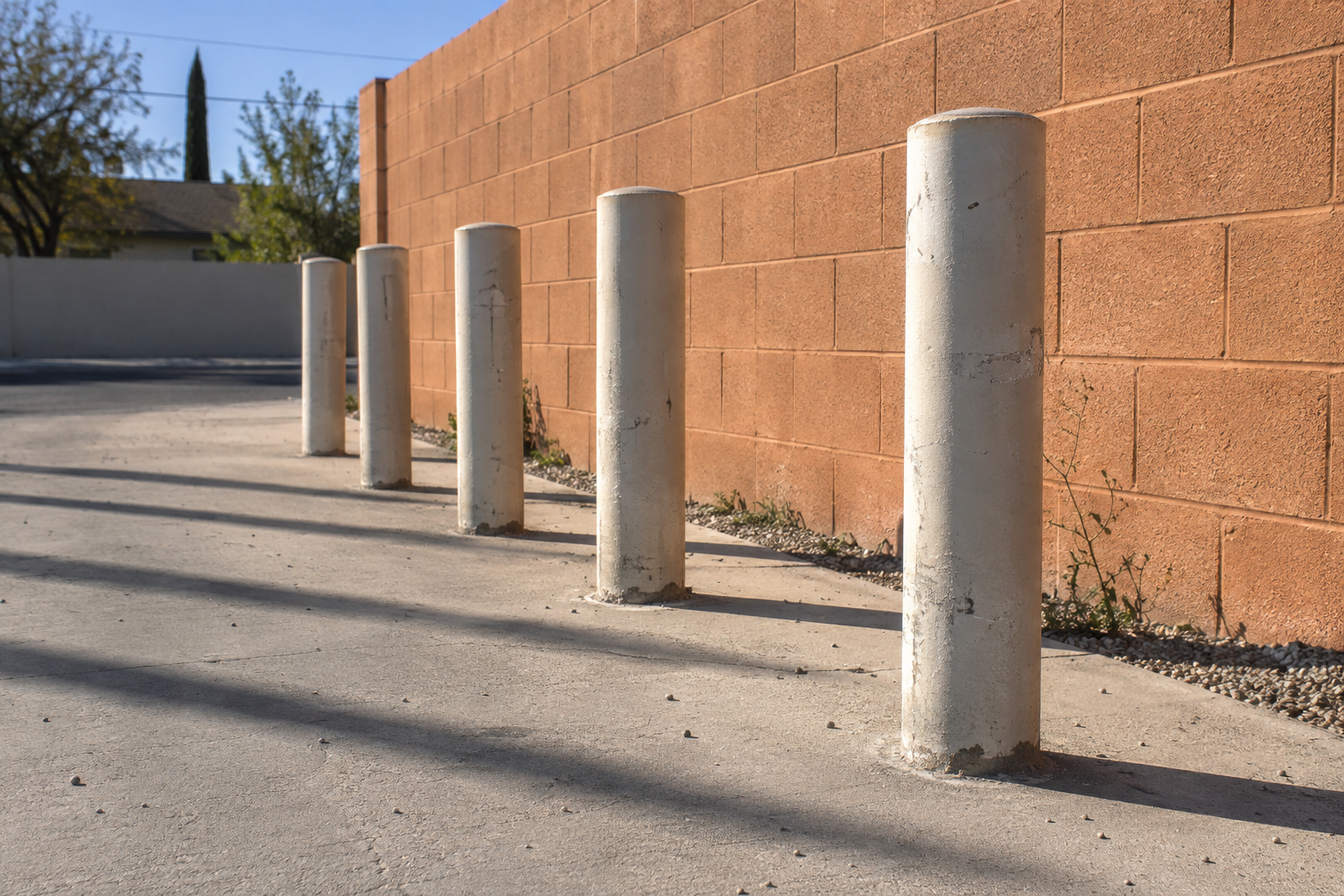 Five off-white bicycle bollards recede beside an orange brick wall, casting long parallel shadows.